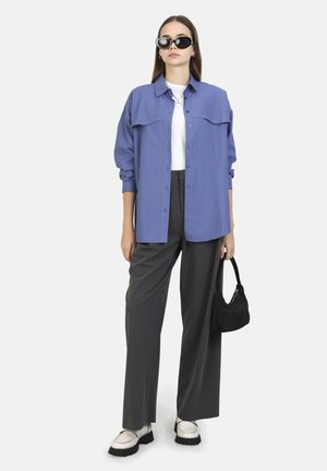 Light purple button-up shirt, white tee, gray wide-leg pants, and black handbag. Chunky white shoes. Black cat-eye sunglasses.