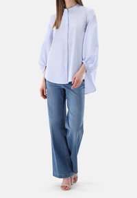 Light blue striped button-up shirt with a mandarin collar and billowy sleeves, paired with wide-leg blue jeans and light-colored sandals.