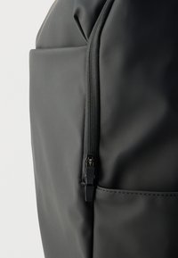 Μαύρο υφασμάτινο σακίδιο με κομψή, λεία υφή, εμφανές φερμουάρ και λεπτομέρεια τσέπης στο πλάι.