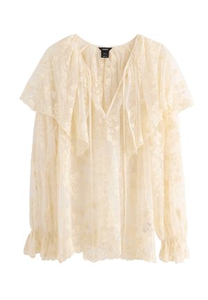 Top in lino di un crema pallido con texture in pizzo floreale, scollatura a V e maniche con pizzo arricciato. Presenta polsini elasticizzati e un delicato motivo floreale.