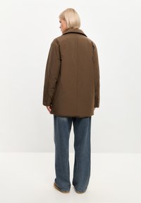 Chaqueta de abrigo marrón con cuello tipo solapa, mangas largas y corte holgado. Combinada con vaqueros de pierna ancha en azul claro y calzado marrón.