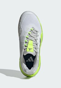 Zapatilla deportiva blanca con una parte superior de malla transpirable, acentos en verde neón y interior negro. Cuenta con una suela texturizada y área de puntera reforzada.