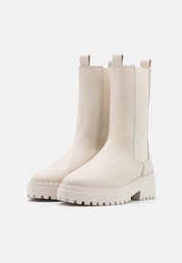 Beige ankle boots with a smooth leather upper, elastic side panels, and a thick, textured platform sole. Features pull tabs for easy wear.