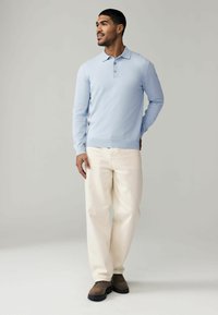 Helles blaues Langarm-Polohemd mit drei Knöpfen, kombiniert mit cremefarbenen Hosen und braunen Schuhen. Schlichtes Design, weiche Textur.
