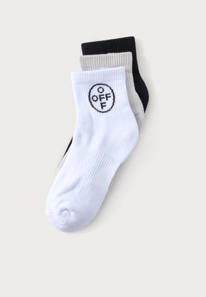 Tres calcetines tobilleros acanalados en blanco, gris y negro, con el calcetín blanco que presenta un logotipo circular "OFF" en negro cerca del puño.