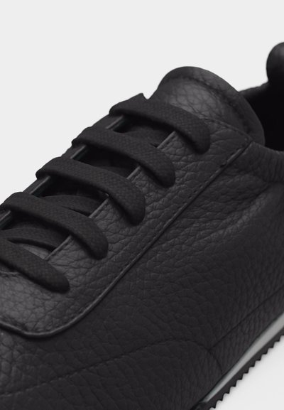 Κοντινό πλάνο μαύρου δερμάτινου αθλητικού παπουτσιού με υφή στην επιφάνεια, μαύρα κορδόνια και ανάγλυφη λεπτομέρεια στη σόλα.