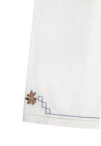 Biała tkanina z małym haftem kwiatowym w kolorze różowym, zielonym i niebieskim w dolnym rogu, akcentowana niebieskim geometrycznym wzorem szycia.