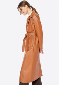 Brauner Leder-Trenchcoat mit tailliertem Schnitt, eingekerbtem Kragen und langen Ärmeln. Besitzt eine glatte Textur und ein elegantes Design.