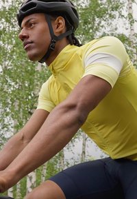 Nahaufnahme eines Radfahrers, der ein gelbes aerodynamisches Trikot mit weißen Ärmeln trägt, das den strukturierten Stoff und eine stromlinienförmige Passform zeigt.