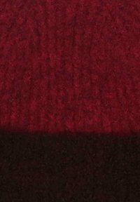 Close-up of a textured fabric with a horizontal division, featuring a dark red upper section and a black lower section.