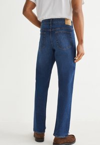 Blue denim jeans with a straight cut, featuring back pockets, a tan leather label on the waistband, and a smooth, soft texture.