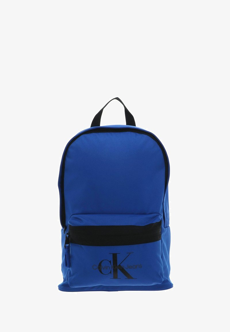 Sac à dos en tissu bleu de forme arrondie, avec une poche avant à fermeture éclair noire et une poignée supérieure. Affiche en bonne place le logo Calvin Klein Jeans.