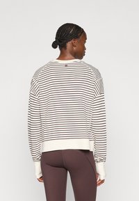 Gestreifter Pullover in Creme und Braun mit langen Ärmeln, Rippbündchen und lockerer Passform, kombiniert mit braunen Leggings.