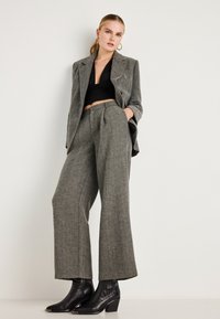 Blazer cinza em padrão pied-de-poule com calças largas a condizer, combinado com uma blusa preta justa e botins pretos de salto.