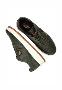 Olive green suede sneakers with white rubber soles, featuring brown accents and textured stitching. Includes logo detail on the side.