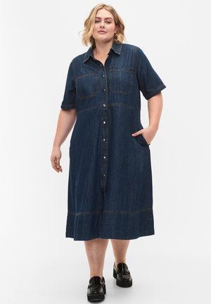 Abito in denim con scollatura a colletto, maniche corte, chiusura frontale con bottoni, due tasche sul petto e una silhouette ad A di lunghezza al ginocchio. Colore blu scuro.