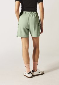 Shorts in cotone verde con cintura elastica, tasche laterali e vestibilità rilassata. Abbinati a calzini rosa a coste e sneakers bianche.