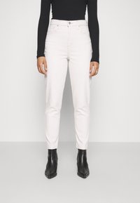 Jeans blancos de cintura alta con corte ajustado, que cuentan con un cierre de botón y cinco bolsillos. Combinados con una blusa negra de manga larga y botas negras hasta el tobillo.