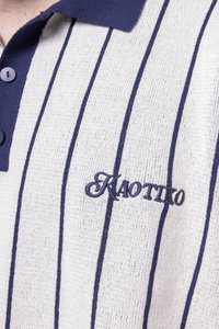 Polo de manga corta con cuello y botones en azul marino, con tela gris claro que presenta rayas verticales en azul oscuro y el logo bordado de "Kaotiko".