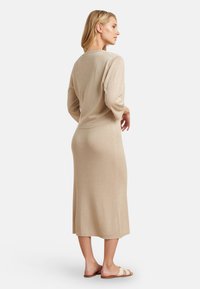 Beige ribbed knit dress with long sleeves, a crew neckline, and a straight silhouette, paired with neutral sandals.