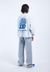 Hellblaues Langarmhemd mit einem grafischen Design in Dunkelblau, das Blumen und Text zeigt. Kombiniert mit hellblauen weit geschnittenen Jeans und blauen Sneakers.