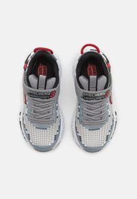 Pár sivých a bielych tenisiek Skechers Mega-Craft 3 s pixlovým dizajnom, sivými šnúrkami a červenými akcentmi, zobrazené zhora na bielom pozadí.