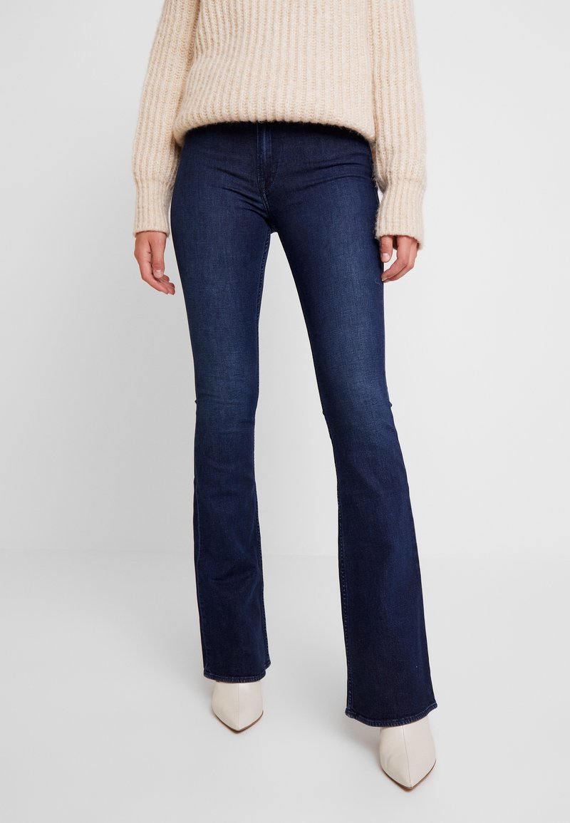 Mörkblå utsvängda jeans i denim med en åtsittande midja och en lätt stretch. Matchas med en ljus beige stickad tröja och krämfärgade klackar.