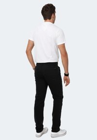 Men's fitted white cotton t-shirt, black denim jeans, white casual shoes. Visible stitching on jeans, short sleeves on t-shirt.