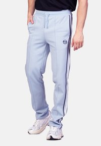 Lichtblauwe joggingbroek met zijstrepen, drawstring taille, logo-detail op de dij en zakken. Zachte stof met een gladde textuur.