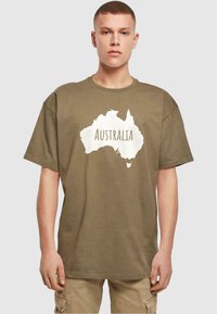 Olijfgroene katoenen t-shirt met een witte silhouet van Australië met het woord "AUSTRALIË" eronder gedrukt. Losse pasvorm, korte mouwen.