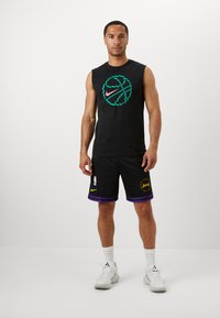 Čierne tielko bez rukávov s grafickou potlačou basketbalovej lopty v zelených a ružových farbách; čierne šortky s fialovými detailami a logom NBA; biele športové tenisky.