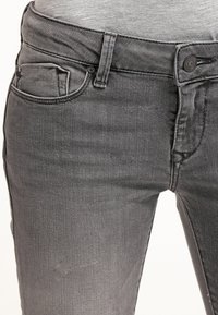 Jeans in denim grigio con un design classico a cinque tasche, dotati di zip e bottone superiore, texture liscia e lieve scolorimento sulle ginocchia.