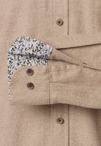 Lys brun button-up skjorte med en struktureret stof, med blomster mønster accent i manchetternes foring og brune plastikknapper.