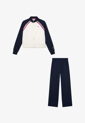 Biała i granatowa kurtka sportowa na zamek z czerwonymi paskami, zestawiona z granatowymi spodenkami sportowymi z elastycznym pasem.