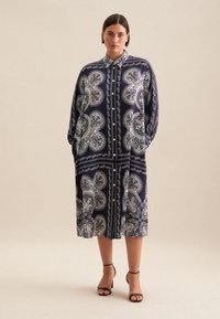 Abito camicia blu navy con motivo paisley, maniche lunghe e chiusura con bottoni. Presenta tasche laterali e una vestibilità ampia, con un orlo all'altezza del ginocchio.