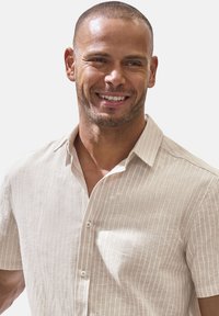 Helles beiges Kurzarmhemd mit einem dezenten vertikalen Streifenmuster, aus einem strukturierten Stoff gefertigt und mit einer Knopfleiste und Kragen ausgestattet.