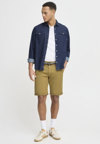 Cămașă din denim de culoare albastru închis, cu mânecă scurtă, două buzunare pe piept, asortată cu pantaloni scurți khaki rulați. Tenisi bej cu accente albe și șosete.