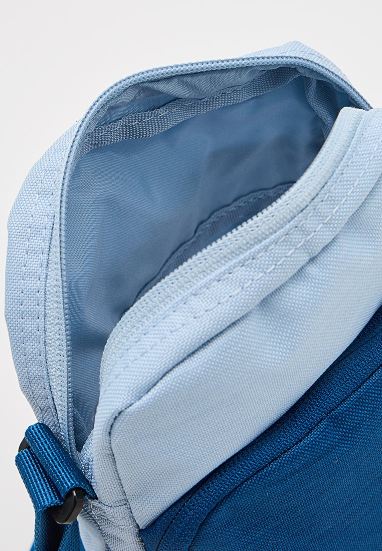 Bolsa de nylon azul claro con apertura con cremallera. Cuenta con un forro interior suave, costuras reforzadas y una correa de ajuste lateral.