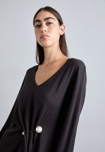 Black knit sweater with a V-neck and long sleeves, featuring a decorative pearl accent at the waist and a soft texture.