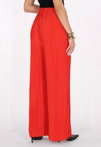 Red pleated wide-leg pants with a high waist and textured fabric. Black high-heeled shoes with pointed toes and studded accents visible.