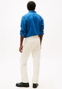 Blaues Denimhemd mit hochgekrempelten Ärmeln, weiße Hose und schwarze Stiefeletten. Fokus auf Stoffstruktur und Knopfdetails des Hemdes.