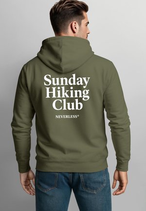 Man wearing olive green hoodie with "Sunday Hiking Club NEVERLESS" text on the back, paired with blue jeans, facing away.