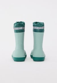 Bottes imperméables vertes avec une finition texturée, un haut pliable en vert foncé, et des accents réfléchissants autour de la cheville. Semelles en caoutchouc robustes.