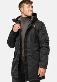 Schwarze gepolsterte Parkajacke mit Kapuze, mit braunen Akzenten, Seitentaschen und einem strukturierten Futter. Sichtbarer Reißverschluss und Druckknopfverschluss.