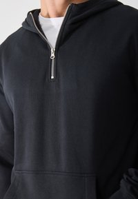Sudadera negra de suave mezcla de algodón, con cierre de media cremallera, un bolsillo tipo canguro en la parte frontal y puños acanalados para un ajuste ceñido.