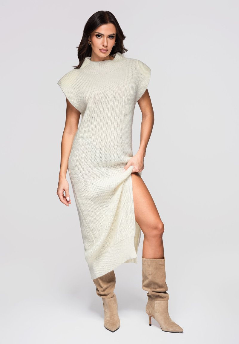 Robe maxi en maille de couleur crème avec un col montant, une fente latérale et des manches courtes. Associée à des bottes beige décontractées montant jusqu'aux genoux.
