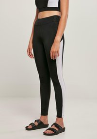 Leggings noirs à taille haute, avec des panneaux latéraux blancs. Confectionnés en tissu extensible, conçus pour le confort et la mobilité, assortis à des sandales noires.