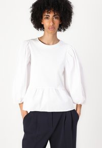 White blouse with short puff sleeves and a gathered waist. Made from a smooth fabric, featuring a rounded neckline and relaxed fit.