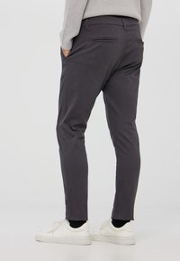 Pantaloni slim-fit grigio scuro realizzati in tessuto morbido, con tasche posteriori e una texture liscia, abbinati a sneakers bianche.
