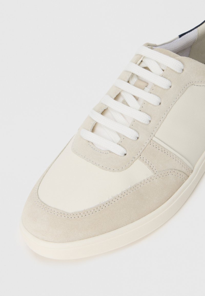Baskets en cuir suédé beige et cuir lisse avec lacets blancs, bout arrondi et subtils détails de couture. Texture douce et design minimaliste.